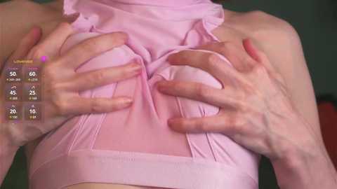 Media: Video of a light-skinned person wearing a pink halter top, hands pressing against the fabric, revealing a cleavage. Background is blurred, with a digital health app overlay showing body measurements.