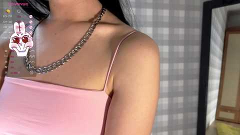 Media: A video of a woman with medium skin tone, wearing a pink spaghetti-strap dress, silver chain necklace, and black hair. Background shows a checkered curtain. Digital filters include a pink bunny face and thermometer icons.