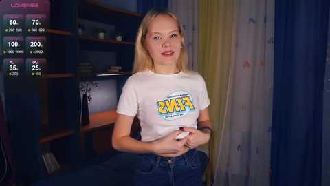 Media: A video of a young, slender, blonde woman in a white \"FIFA\" t-shirt, standing in a dimly lit room with a TV screen displaying game stats.