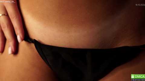 Media: Close-up video of a person's lower torso, focusing on a tan line where black underwear is pulled down slightly, revealing a smooth, tanned skin tone. The background is dimly lit, highlighting the contrast.