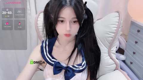 Media: Video of an Asian woman with long black hair in a sailor schoolgirl outfit, sitting on a bed with plush toys.