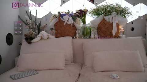 Media: Video of a modern, white living room with plush couches, floral arrangements, and a decorative basket, with a social media watermark in the corner.