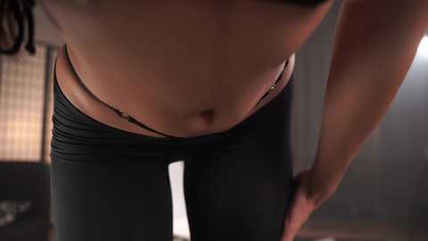 Media: A video of a woman in black leggings, with a side view, showcasing her toned midriff and lower abdomen.