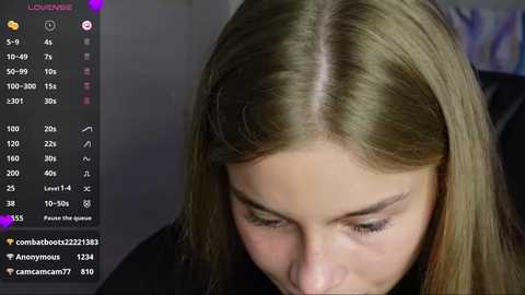 Media: Video of a close-up of a young woman with long, straight, light brown hair, looking down. The background is blurred, and the image includes a streaming overlay with chat messages.