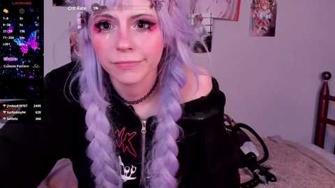 Media: Video of a young woman with lavender hair in twin braids, wearing a black hoodie, pink eye makeup, and a black choker. She's in a bedroom with posters and a computer screen displaying streaming software.