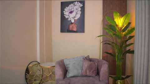 Media: Video of a modern living room with a pastel pink couch, a tall green plant, a gold geometric pillow, a beige wall, and a large floral painting above.