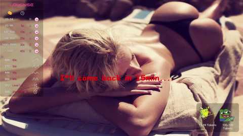 Media: Video of a blonde woman with fair skin, lying face down on a beach, wearing black thong bikini bottoms. Text overlay reads: \"I'm coming back in 2 hours.\