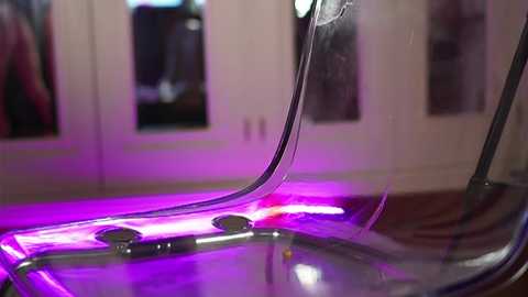 Media: Video of a clear acrylic chair with a smooth surface, lit by purple LED lights. The background features a blurred closet with hanging clothes. The scene has a modern, minimalist aesthetic.