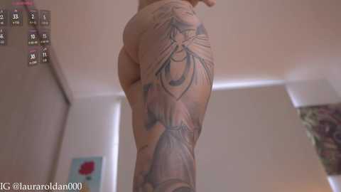 Media: Video of a tattooed person's lower back, featuring a detailed black and grey tattoo of a woman with wings, in a dimly lit room.