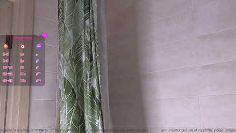 Media: Video of a bathroom showing a green, leaf-patterned shower curtain and beige tiled walls. A digital display on the left reads \"Luxury Shower\" with buttons and a purple light.