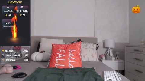 Media: Video of a modern bedroom with a gray bed, orange \"HELLO FALL\" pillow, a pumpkin on the nightstand, and a white lamp. Live stream overlay shows a thermometer and heart rate monitor.