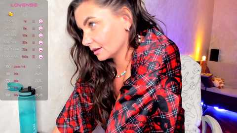 Media: A video of a woman with long dark hair in a red plaid shirt, seated at a desk with a calendar, laptop, and a decorative lamp.