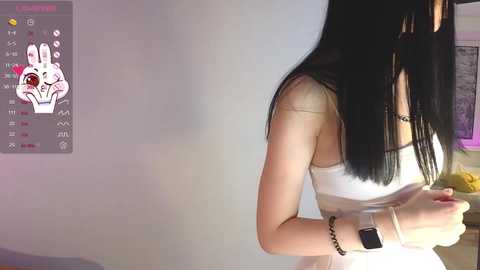 Media: A video of a woman with long black hair, wearing a white sleeveless dress, standing indoors. She has a white Apple Watch on her wrist. A digital overlay shows a cartoon rabbit.