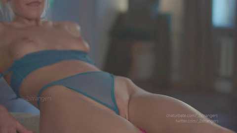 Media: A video of a light-skinned woman with blonde hair, wearing a turquoise bra and matching thong, reclining on a bed in a dimly-lit room.