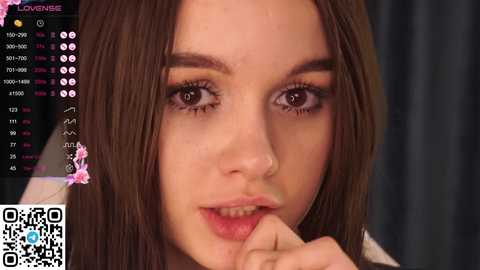 Media: Video of a young woman with fair skin, straight brown hair, and brown eyes, biting her lower lip, set against a dark background.