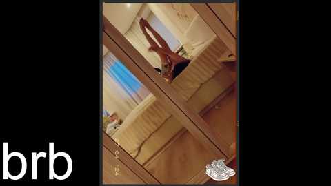 Media: Video of a mirrored bedroom with a person in the background, wearing a black shirt, reflected in the mirror. The room has a bed, curtains, and a wooden floor.