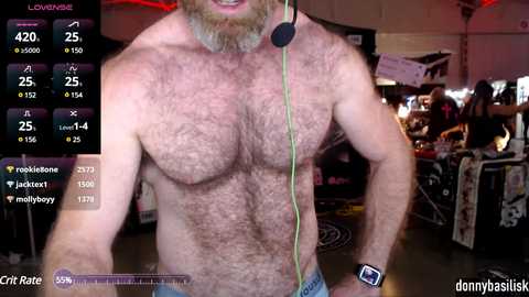 Media: Video of a shirtless, muscular, bearded man with a green headphone cord around his neck, standing in a dimly lit room with various objects in the background.