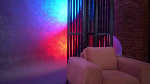 Media: Video of a dimly lit room with a beige armchair facing a textured brick wall. The background features vertical metal bars with vibrant blue and red LED lights creating a striking, futuristic atmosphere.