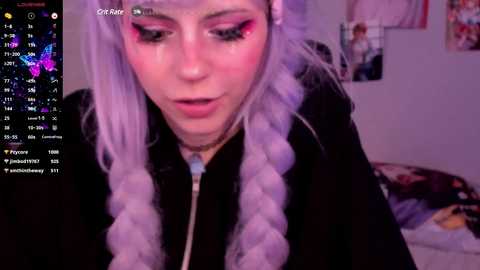 Media: A young woman with long, lavender-dyed braids and colorful eyeshadow sits indoors, looking down. The background shows a bed with posters and a calendar displaying April 2022.