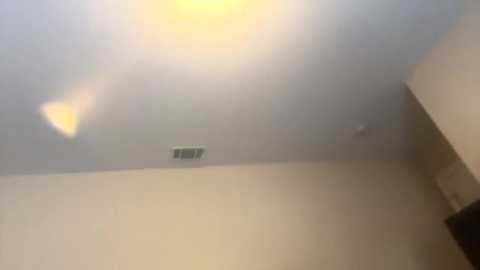 Media: A video of a dimly lit, beige-colored room with a ceiling fan and vent, showing a soft, blurred ambiance.