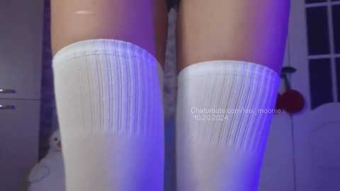 Media: Video of a woman's thighs clad in white, ribbed thigh-high stockings, lit by purple and blue lighting, with a watermark in the center.