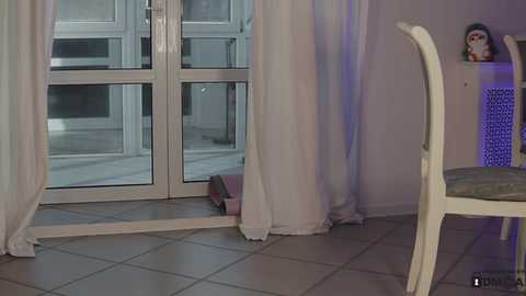 Media: A video of a bright, modern living room with large glass doors, white curtains, tiled floor, and a white chair.