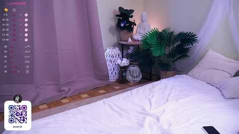 Media: A video of a serene bedroom featuring a white bed with a white comforter, a white and black patterned vase, and a large green potted plant. The background includes a calendar and a decorative Buddha statue.