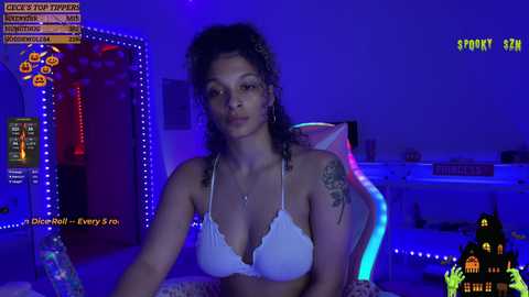 Media: Video of a young woman with medium skin tone and curly hair, wearing a white lace bra, in a dimly lit room with blue neon lighting.