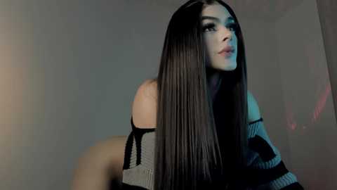 Media: A video of a young woman with long, straight, dark hair and fair skin, wearing an off-shoulder, striped top, gazing thoughtfully to the side.