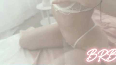 Media: A blurred, soft-focus video of a nude woman kneeling, holding a white lace bra, with a pink heart-shaped watermark in the corner.