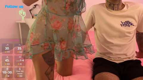 Media: A video of a person in a sheer floral nightgown and a man in a white T-shirt, both seated on a pink bed.