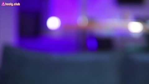 Media: A blurred video with purple and white bokeh lights in the background, featuring a dimly lit room with indistinct furniture. The image lacks focus and clarity.