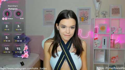 Media: Video of a young woman with long brown hair, wearing a light blue crop top with a black cross design. Background features pink neon lights and various posters. Live stream overlay with stats.