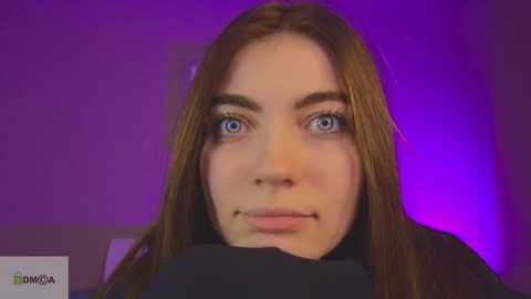 Media: Video of a young Caucasian woman with blue eyes, long brown hair, and fair skin, wearing a black top, against a purple background.