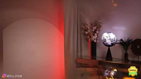 Media: Video of a modern, minimalist room with a large, lit, spherical globe on a shelf; white orchids in a vase; and a red spotlight illuminating a white wall.