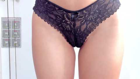 Media: Video of a woman's lower torso in black lace panties, featuring intricate floral patterns. The background is a white room with medical equipment, including a scale, suggesting a clinical setting.