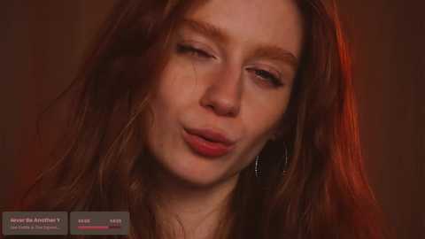 Media: Video of a fair-skinned woman with long, wavy brown hair, puckered lips, and subtle makeup, set against a warm, reddish-brown background.