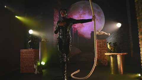 Media: A CGI still from \"The Dark Knight Rises,\" featuring a large, menacing Bane in a black, rubbery suit, grappling hook, and an ominous moon backdrop.