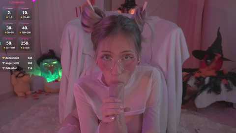 Media: Video of a young woman with light skin and blonde hair, wearing a sheer white top, blowing bubbles in a dimly lit room decorated with Halloween-themed decor.