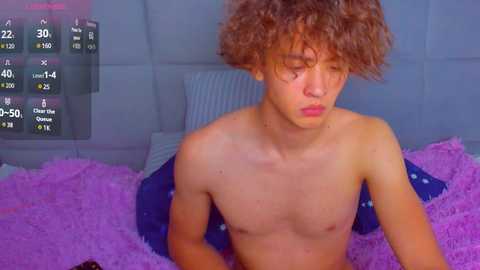 Media: Video of a shirtless, curly-haired, slim young man with fair skin, lying on a purple, fluffy bedspread, looking down, with a digital temperature display on the left.