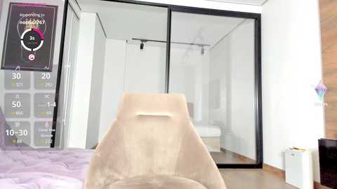 Media: Video of a modern, minimalist bedroom with a beige chair in the foreground, a large walk-in closet with mirrored doors in the background, and a digital thermometer on the left.