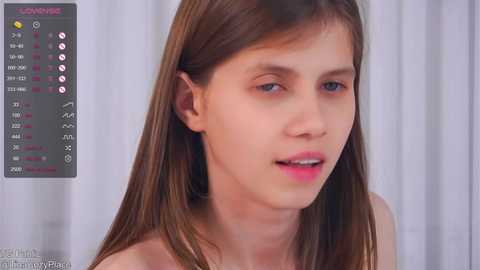 Media: A close-up video of a young Caucasian woman with straight, light brown hair, light skin, and pink lips. She wears a pink top. The background features white curtains.