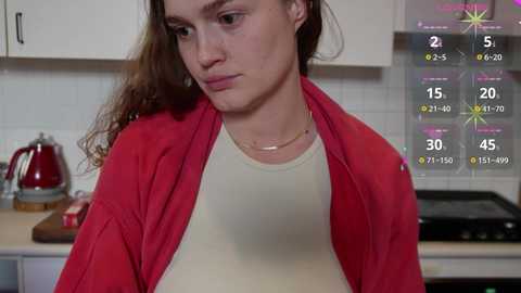 Media: Video of a young woman with long brown hair, wearing a red jacket over a beige shirt, standing in a kitchen with white cabinets, a kettle, and a stove. An AR weather app overlay shows temperature and weather details.