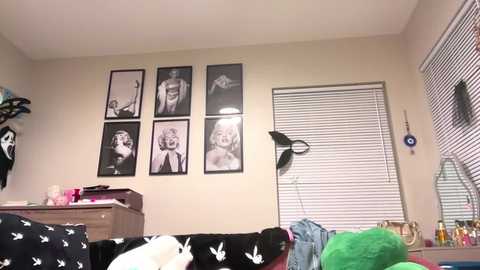 Media: Video of a cluttered bedroom with beige walls, Marilyn Monroe posters, a black Playboy bunny bedspread, a green towel, a desk, and a window with blinds.