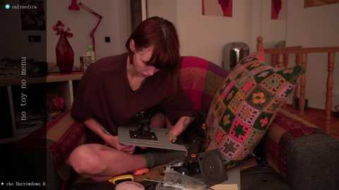 Media: A video of a middle-aged woman with short brown hair, in a dark t-shirt and green socks, fixing a TV set on a couch with a colorful quilt.