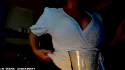 Media: Video of a person wearing a white, textured dress, blending into a dimly lit background. The dress is loose-fitting, and the person is holding a glass, creating a mysterious, almost ghostly effect.