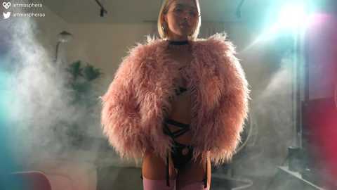 Media: Video of a slender, blonde woman in a pink, fluffy fur coat and black lingerie, standing in a foggy, dimly-lit room with studio lights.