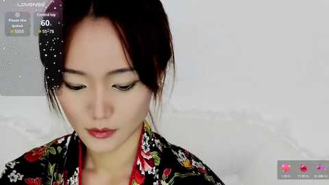 Media: Video of an Asian woman with fair skin, dark hair, and wearing a floral kimono, looking down with a serene expression, against a plain white background.