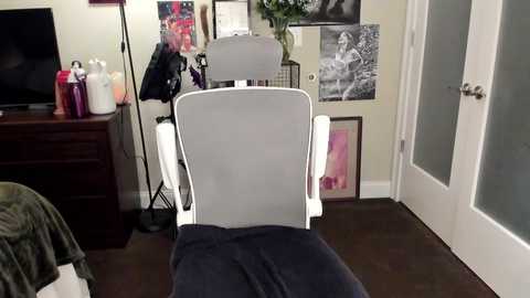 Media: A video of a modern, minimalist home office with a white ergonomic chair, a black TV on a dark wooden stand, and framed black-and-white photos on cream walls.