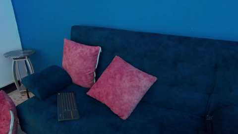 Media: A video of a teal sofa with two pink cushions and a wooden tray on a blue wall, featuring a minimalist, modern interior design.